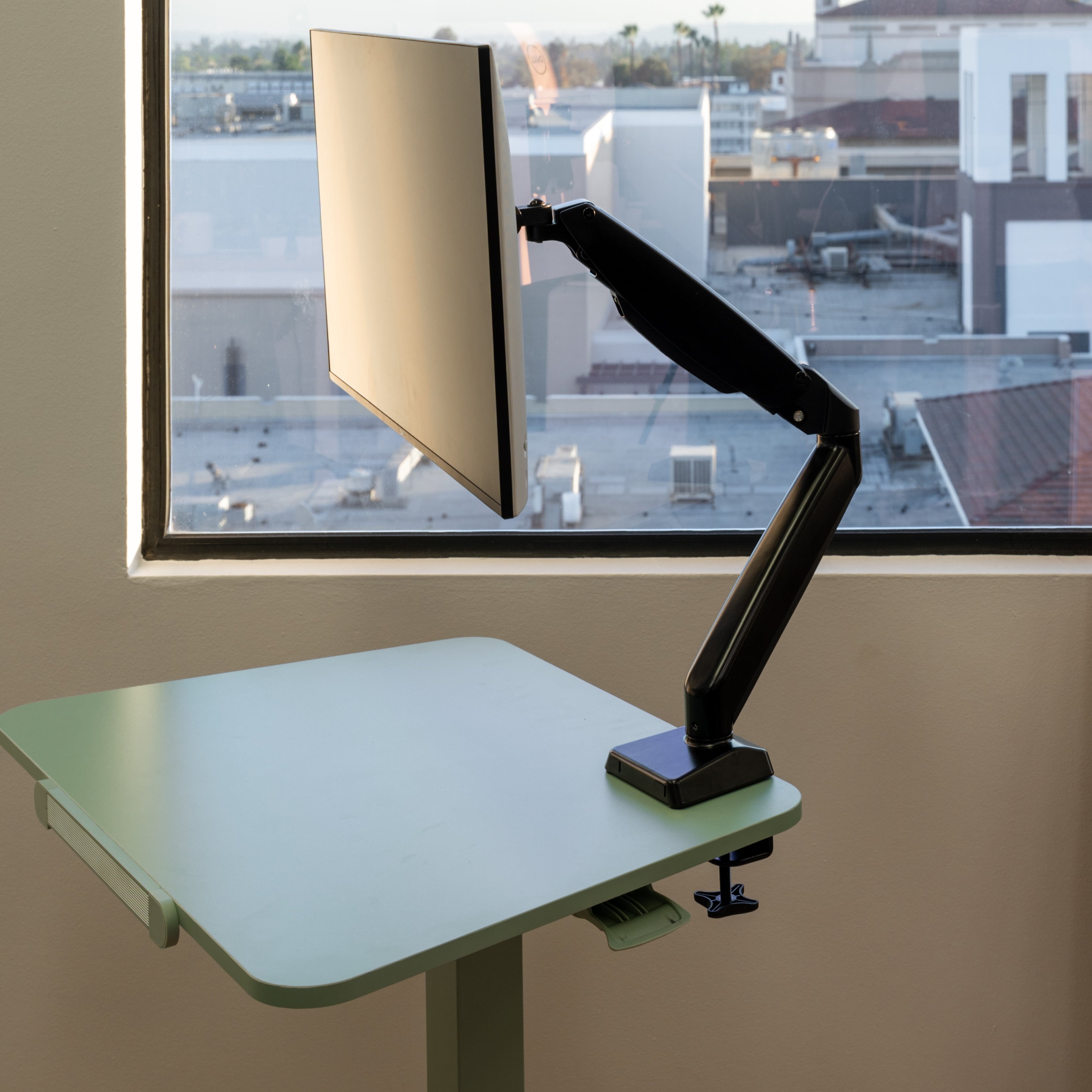 Adjustable monitor arm in a room with a window view of buildings