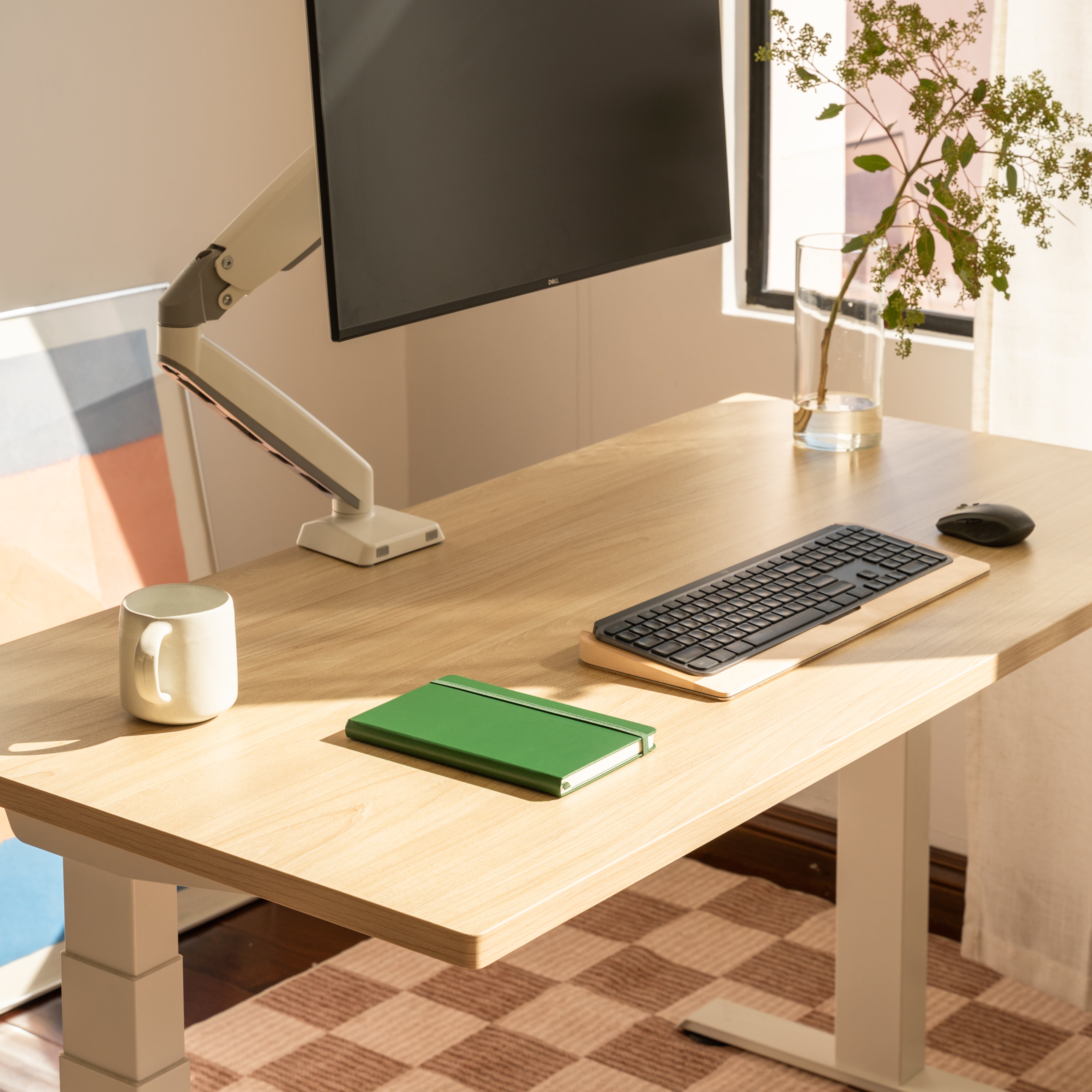 Modern office desk setup with a computer monitor, keyboard, mouse, mug, and notebook.