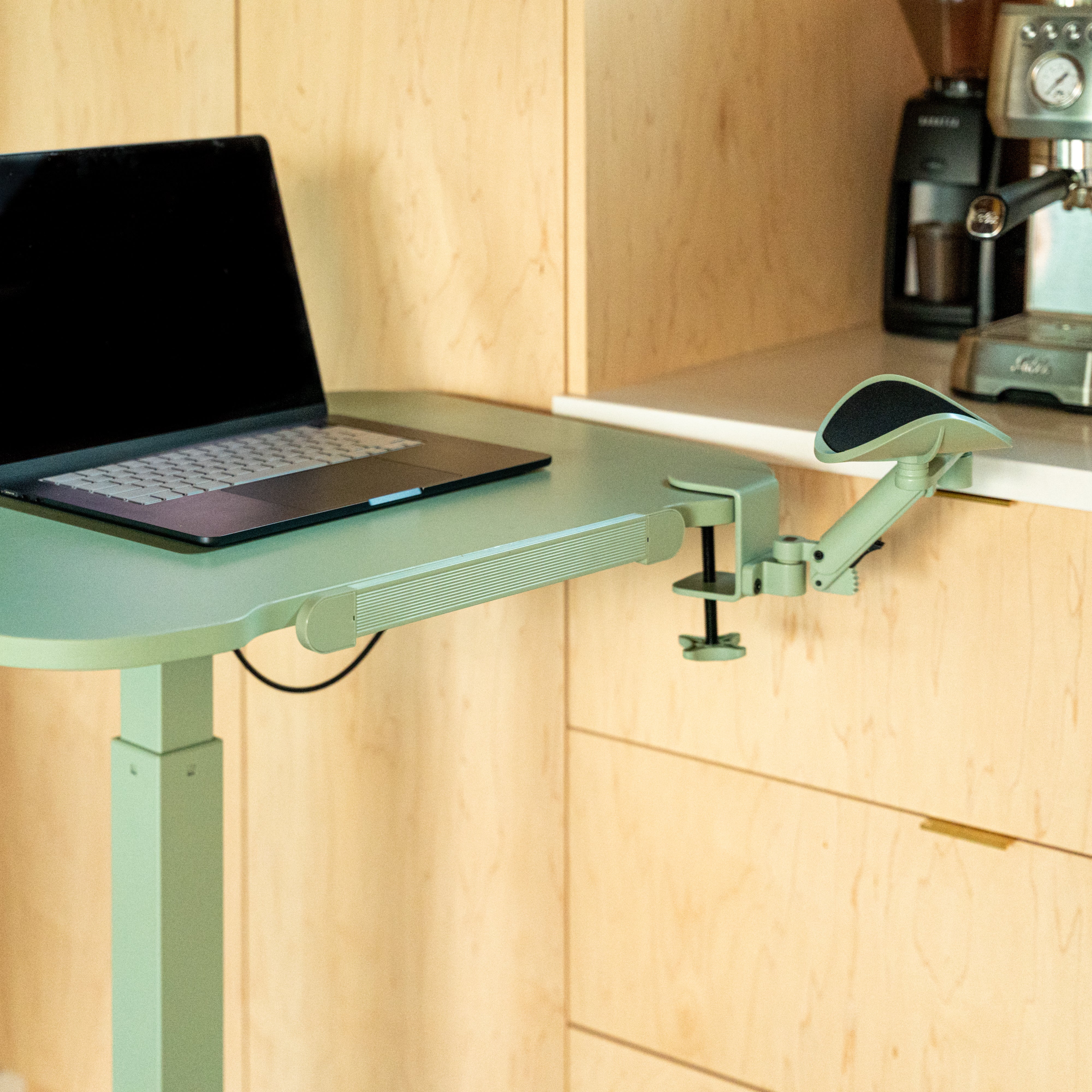 Laptop on a adjustable stand in a kitchen setting with wooden cabinets and appliances.