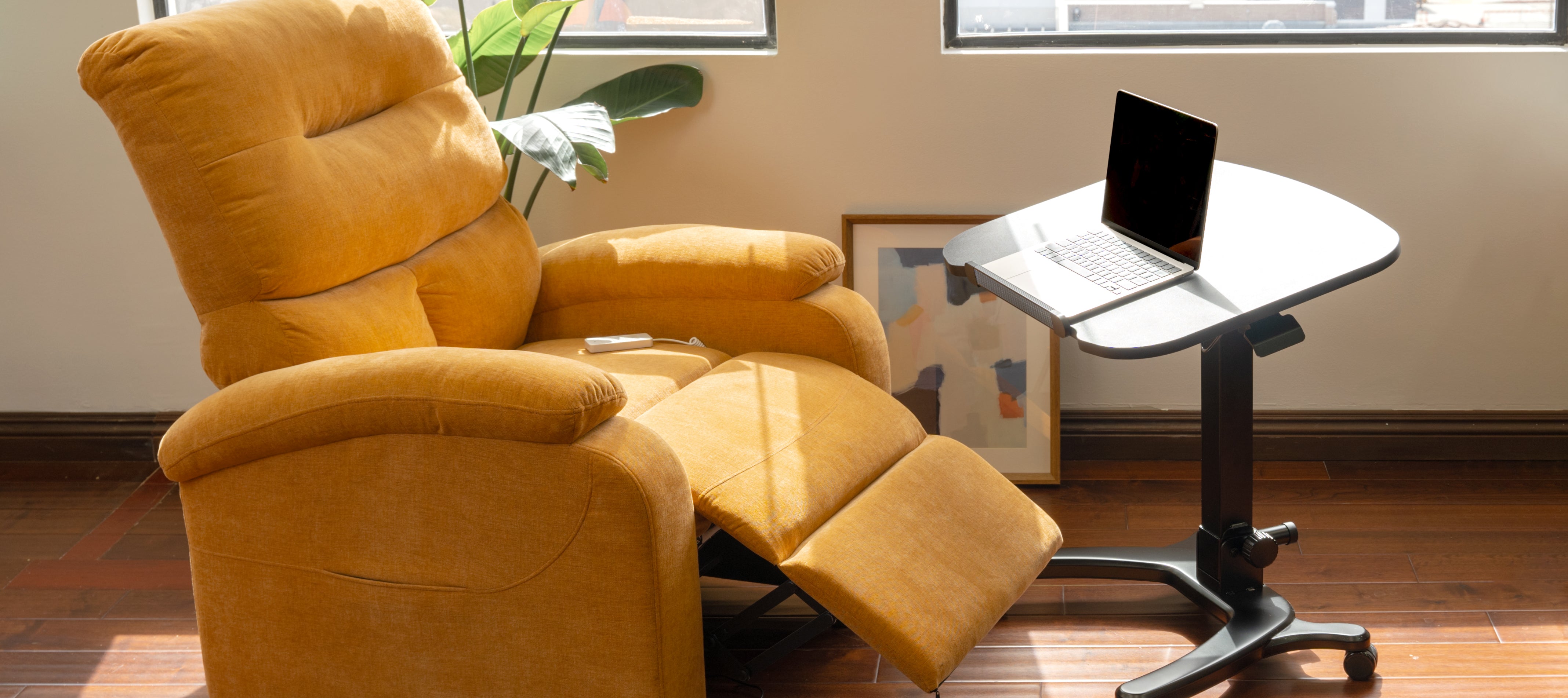 Yellow recliner chair next to a small table with a laptop in a room with a window and plant.