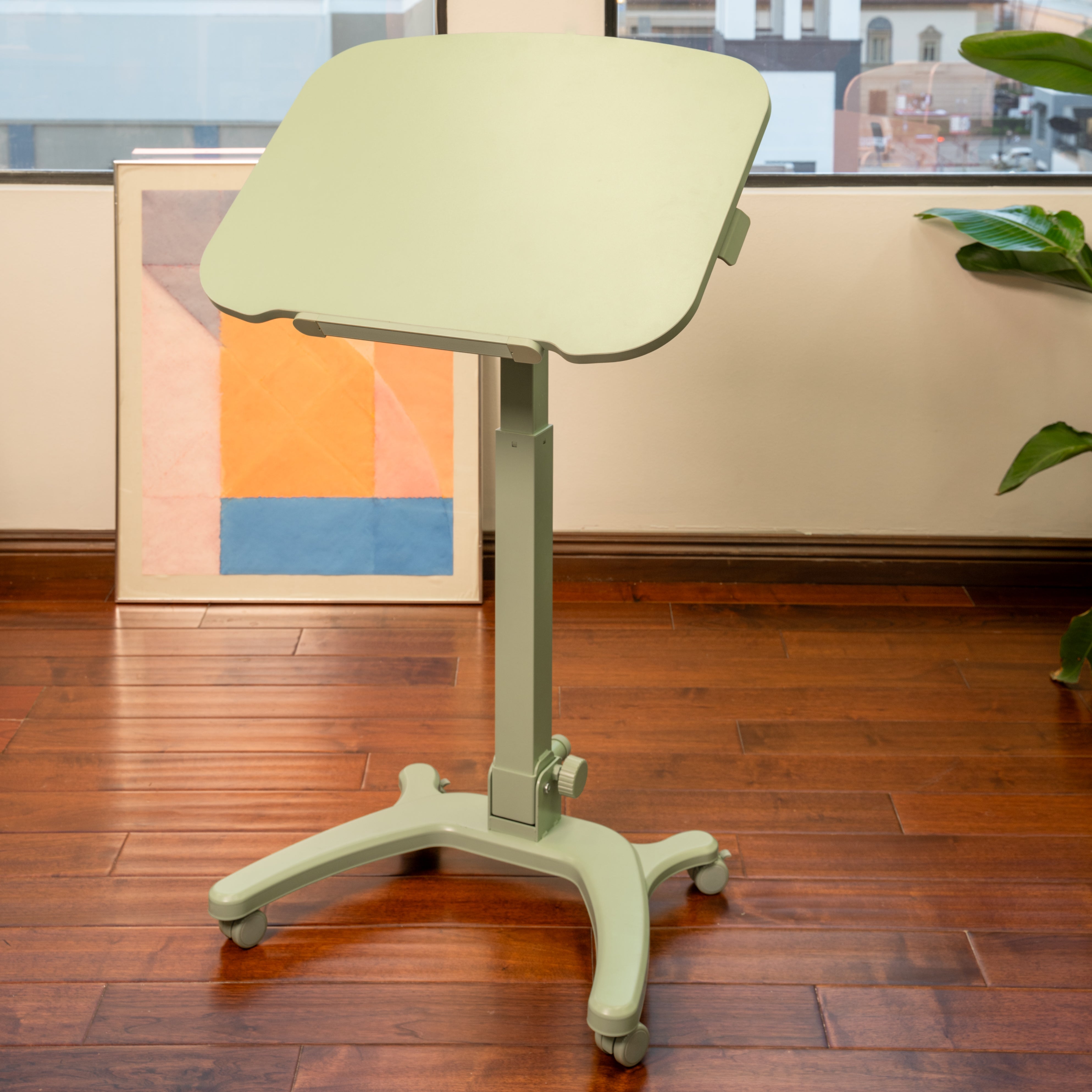 Adjustable sage desk in a room with wooden floor and artwork on the wall