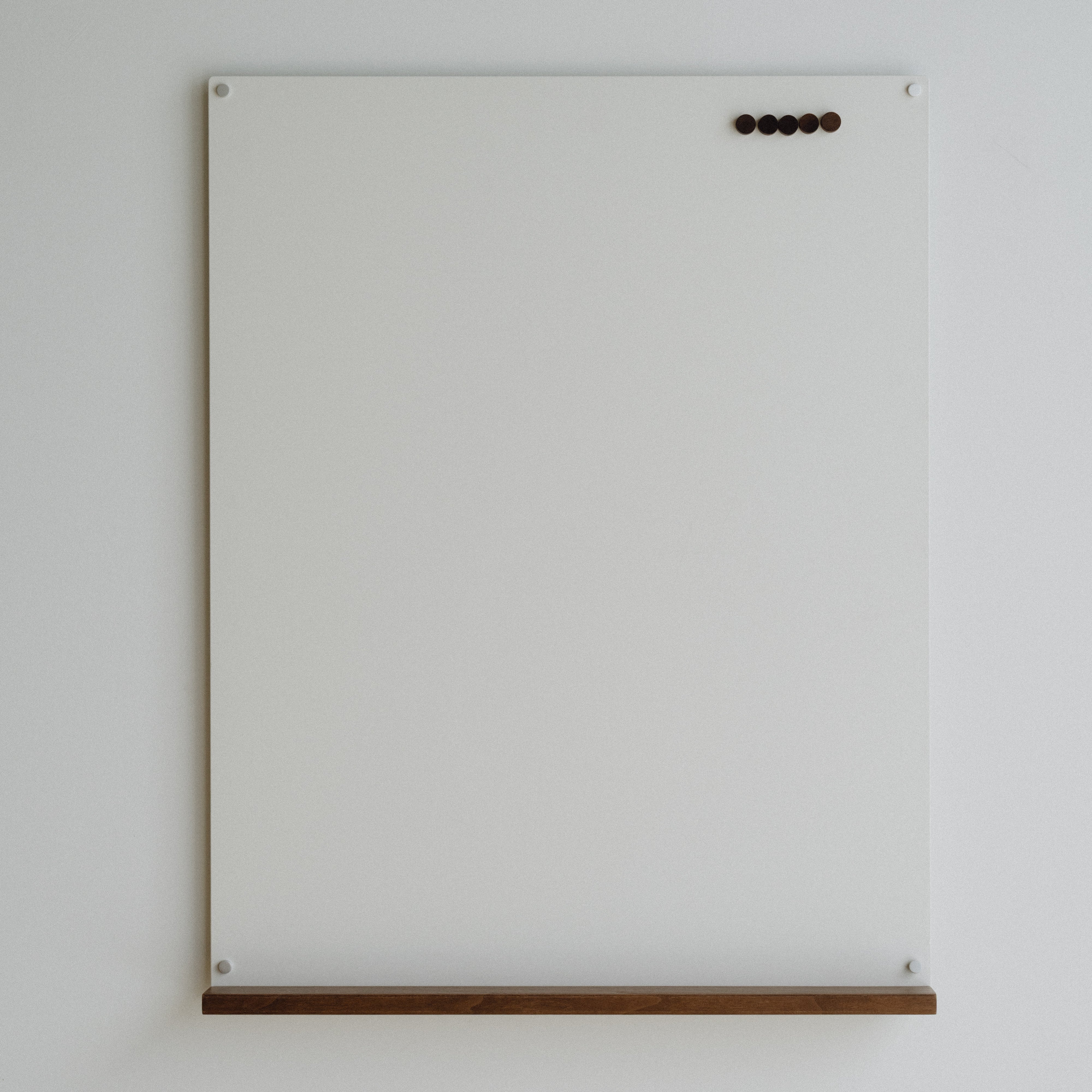 White magnetic board with wooden shelf on a light gray wall