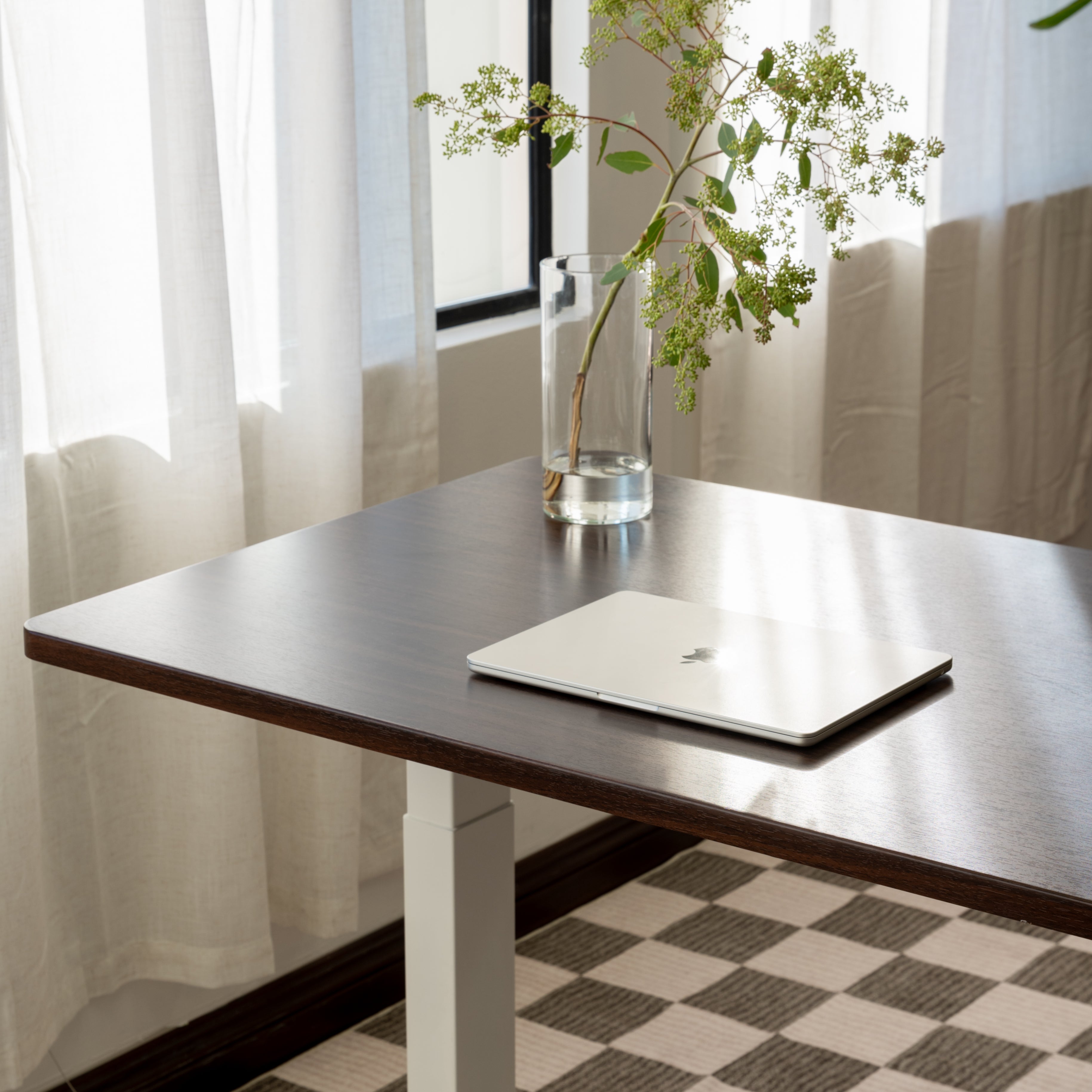 Laptop on a walnut standing desk with a vase of flowers in the background