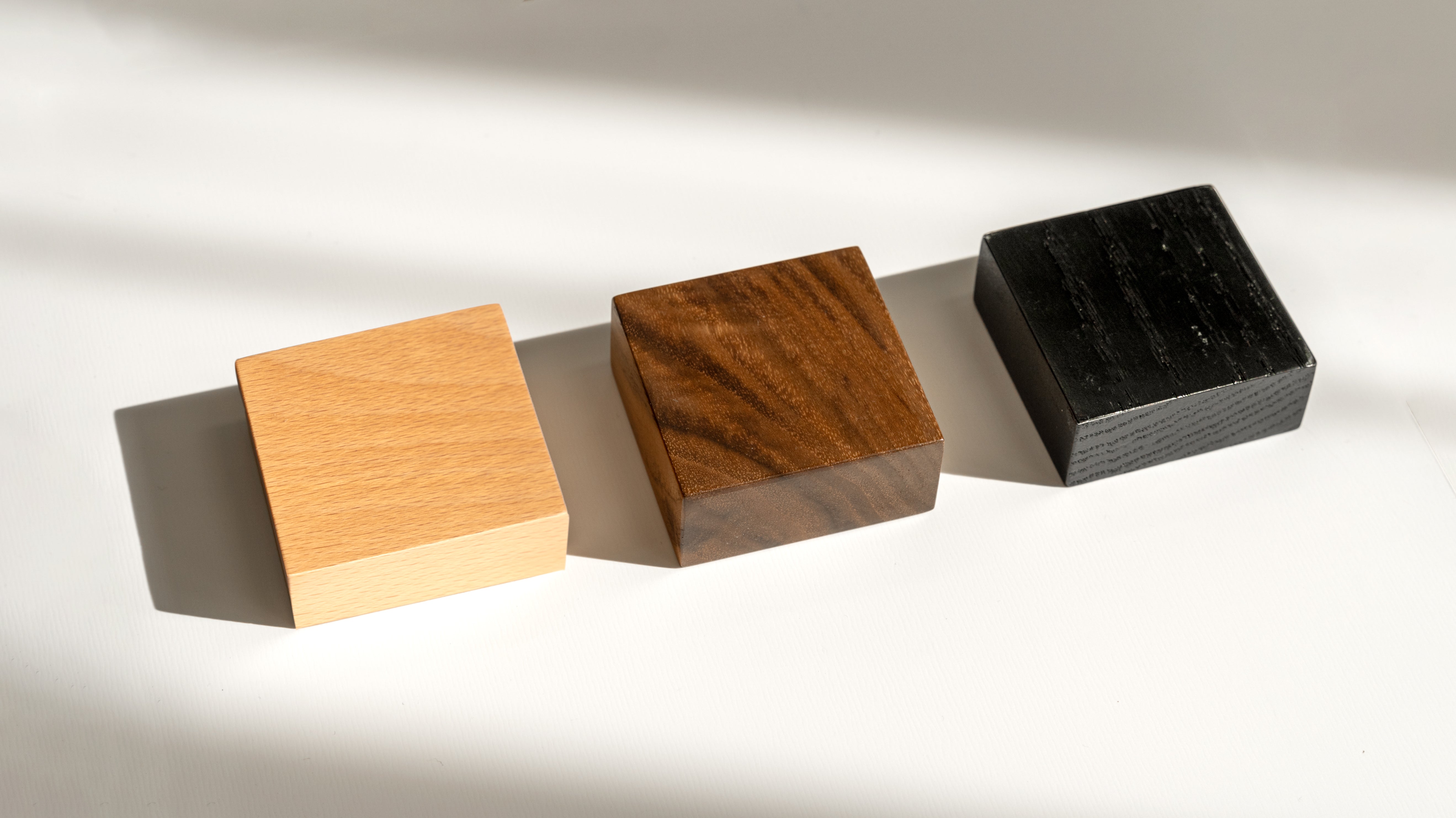 Three square wooden samples in different colors on a neutral background