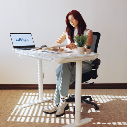 Woman sitting at LiftSync Clear Plus ultra glass standing desk while reading a book