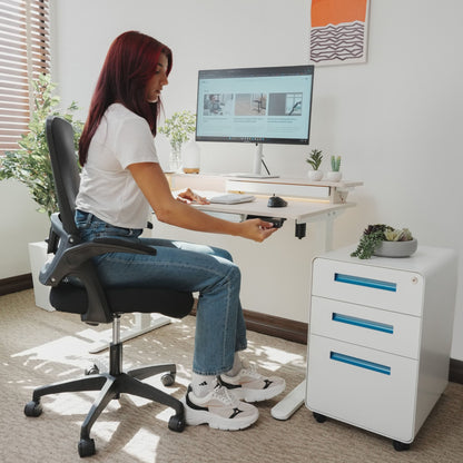 Woman sitting at LiftSync Shelfy electric standing desk with LED lighting, built-in shelf, storage drawer