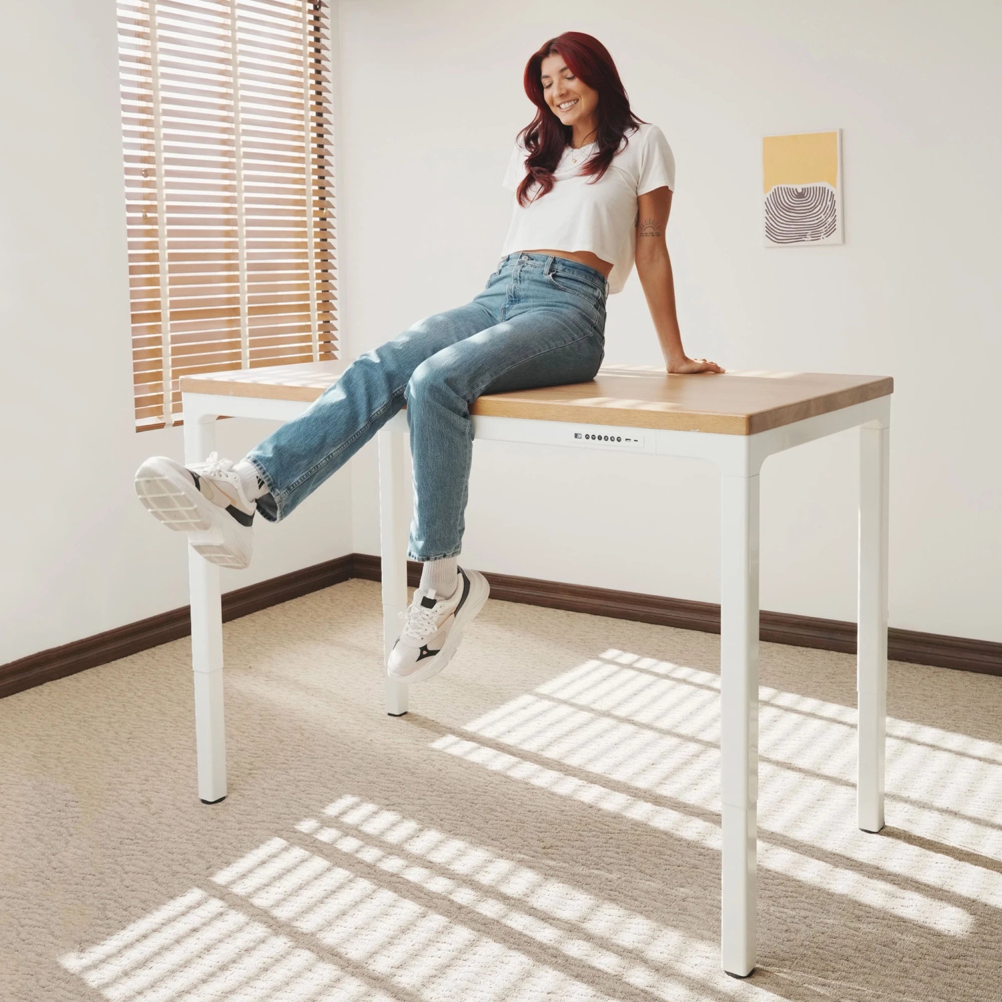 Woman sitting on LiftSync Quad Pro standing desk featuring solid wood top with four motors and four legs