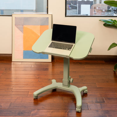 sage adjustable desk with a laptop on a wooden floor in an office setting.