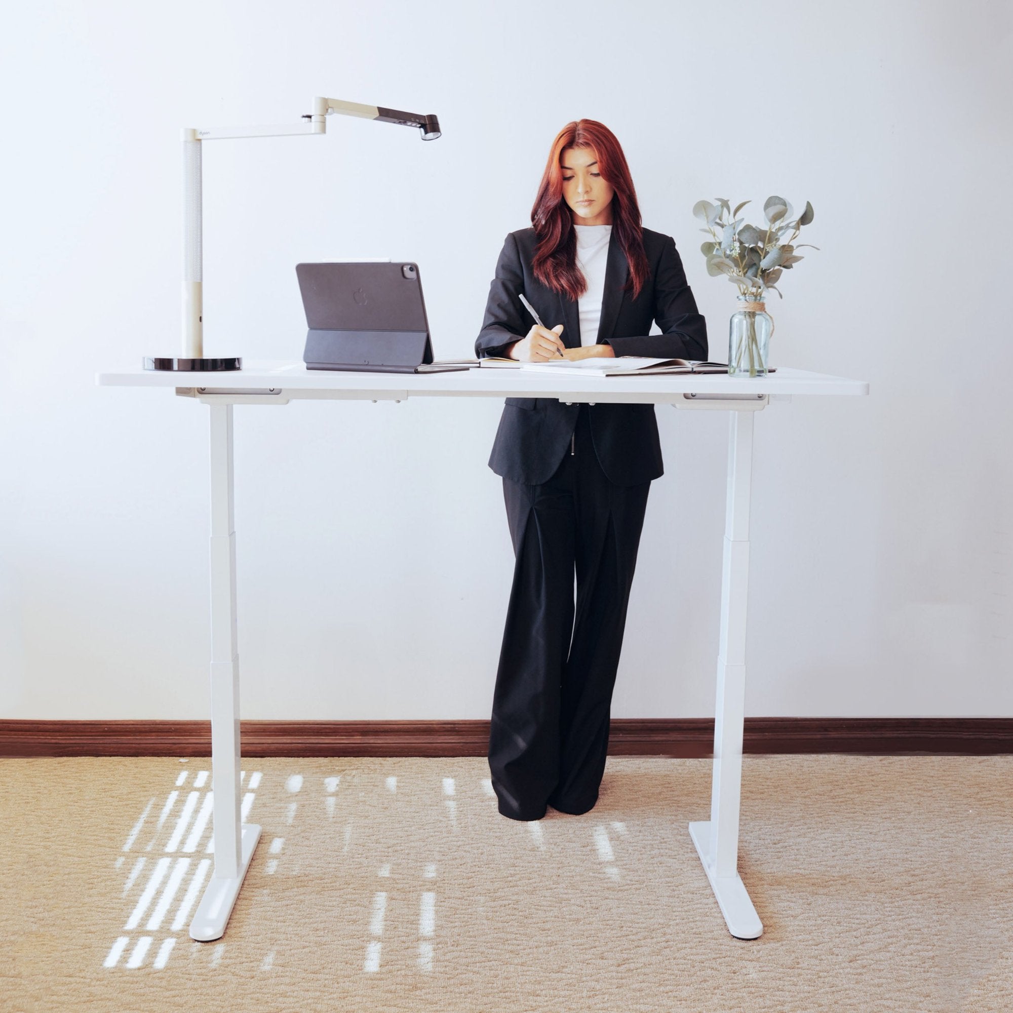 woman standing at LiftSync Pro electric standing desk with white desktop and white desk frame