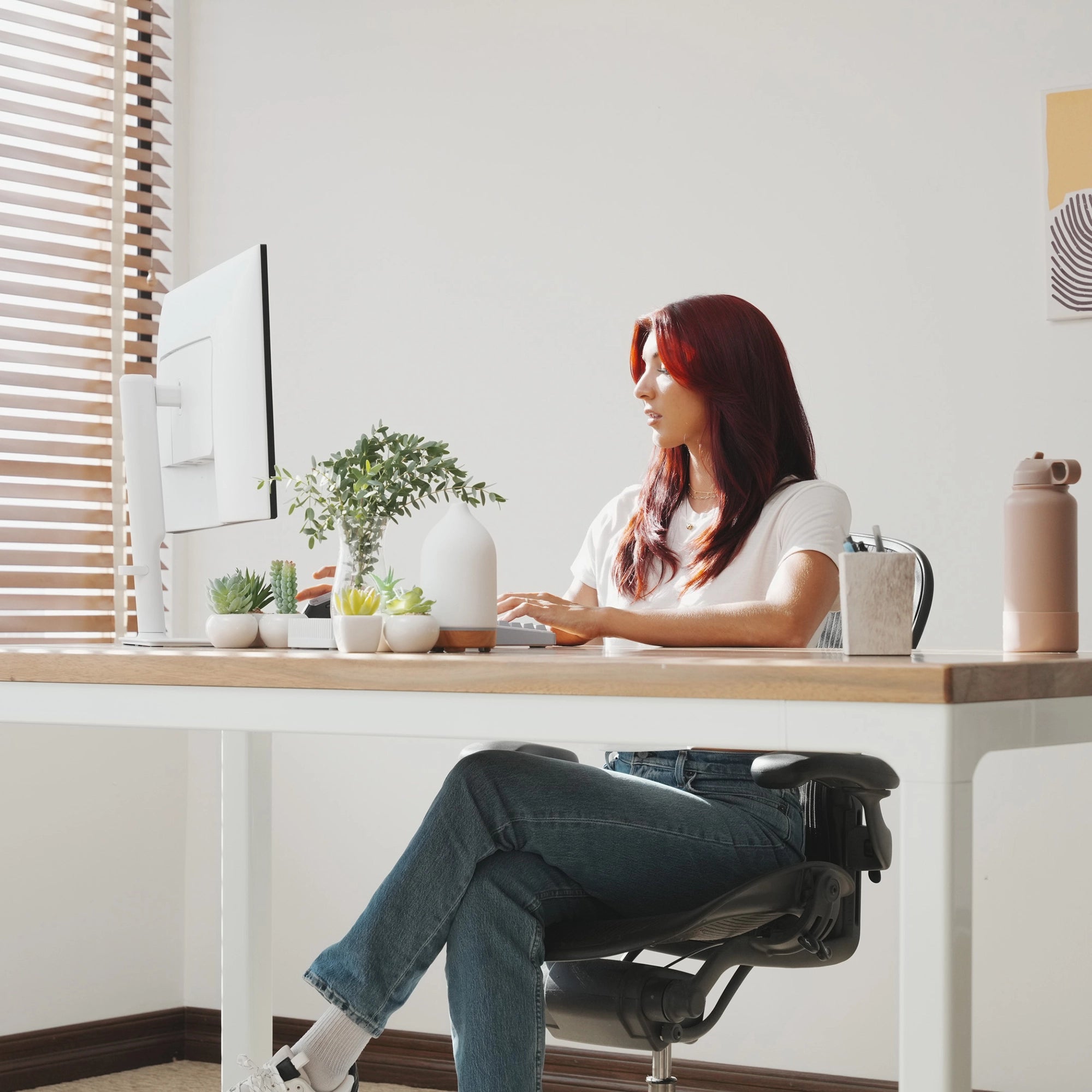 Woman sitting at LiftSync Quad Pro standing desk featuring solid wood top with four motors and four legs