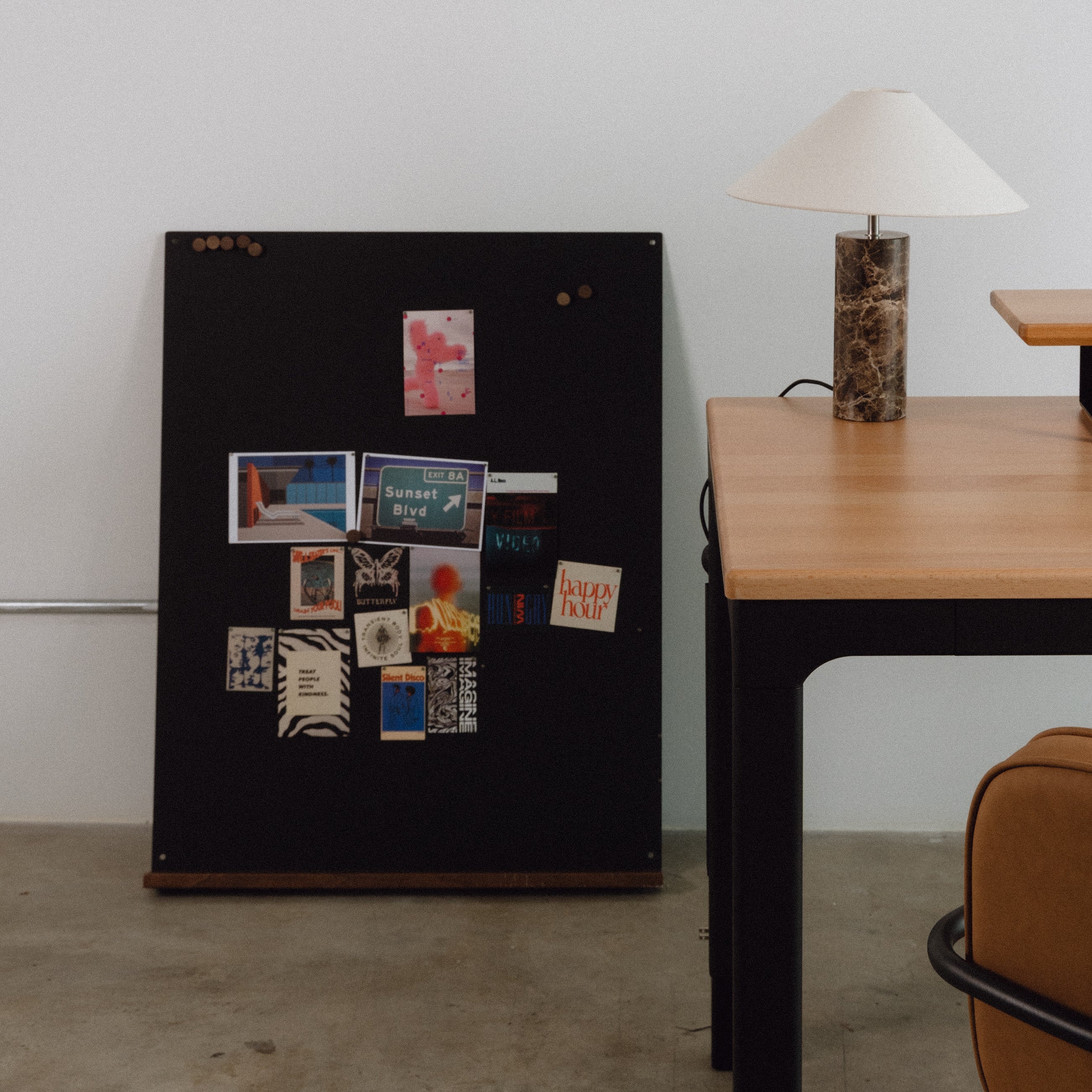 Black magnetic board with various small posters on a white wall next to a wooden table.