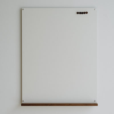 White magnetic board with wooden shelf on a light gray wall