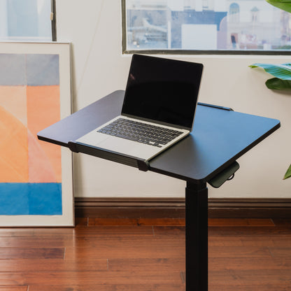 Laptop on a adjustable stand in a room with framed artwork on the wall.