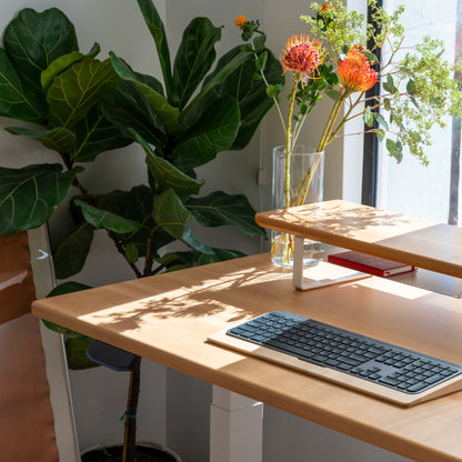 Solid wood desktop standing desk with keyboard, vase of flowers, and plants in a bright room.