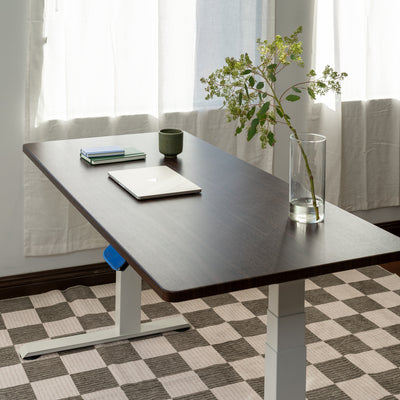 Adjustable desk with a laptop, books, and a vase on a checkered floor.