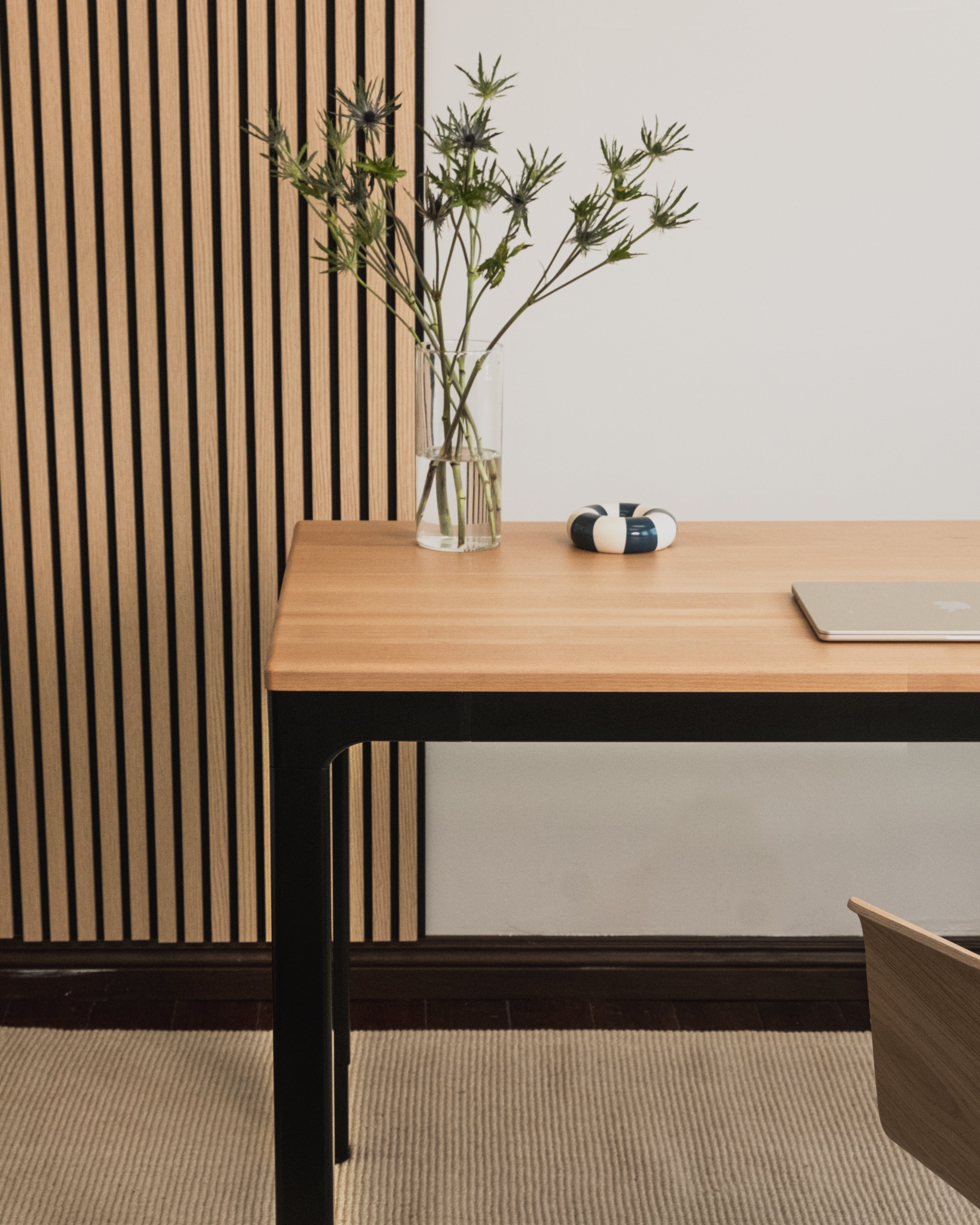 Wooden desk with a vase of dried plants against a striped wall.