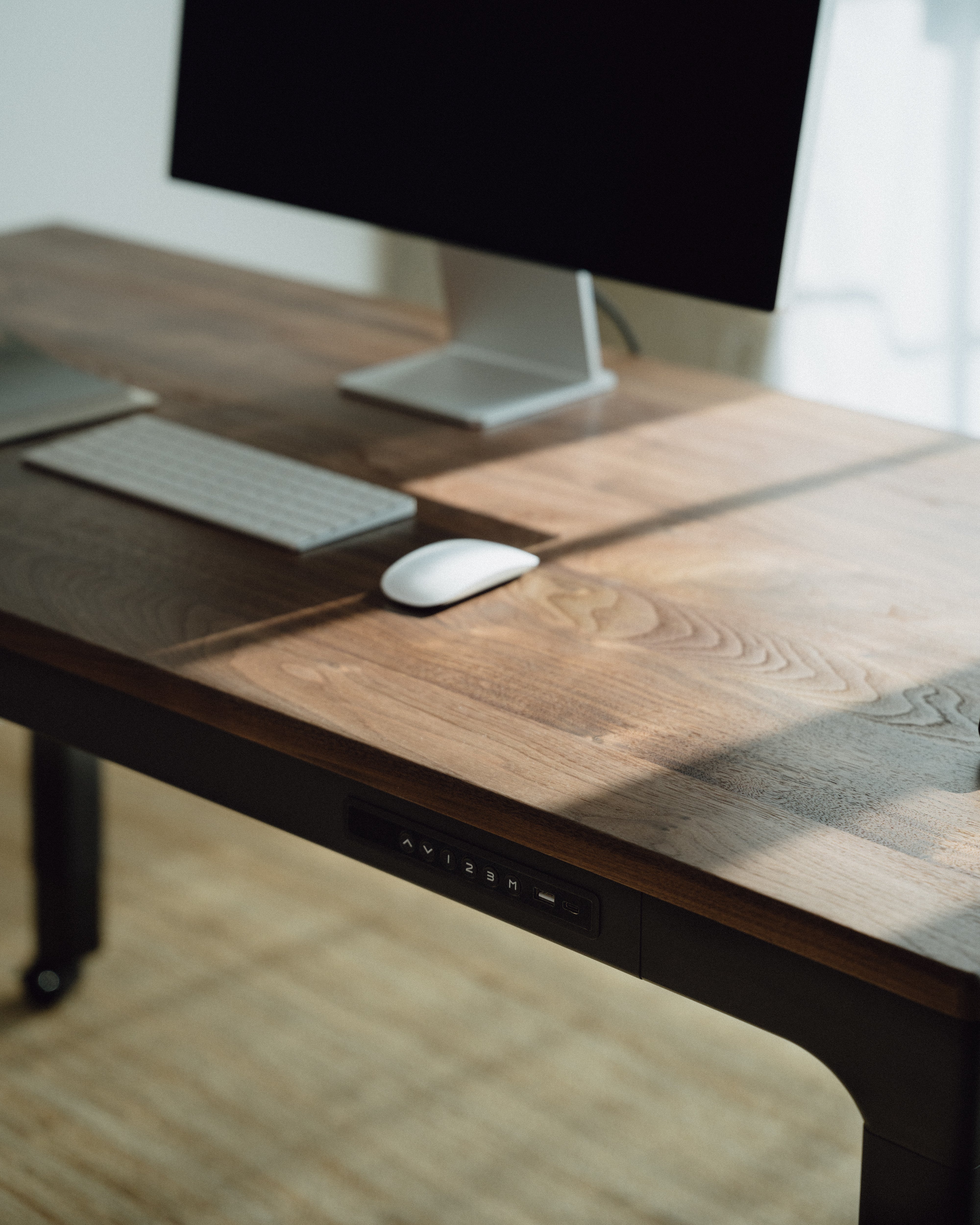 walnut desktop standing desk with computer monitor, keyboard, and mouse on a light wood floor.