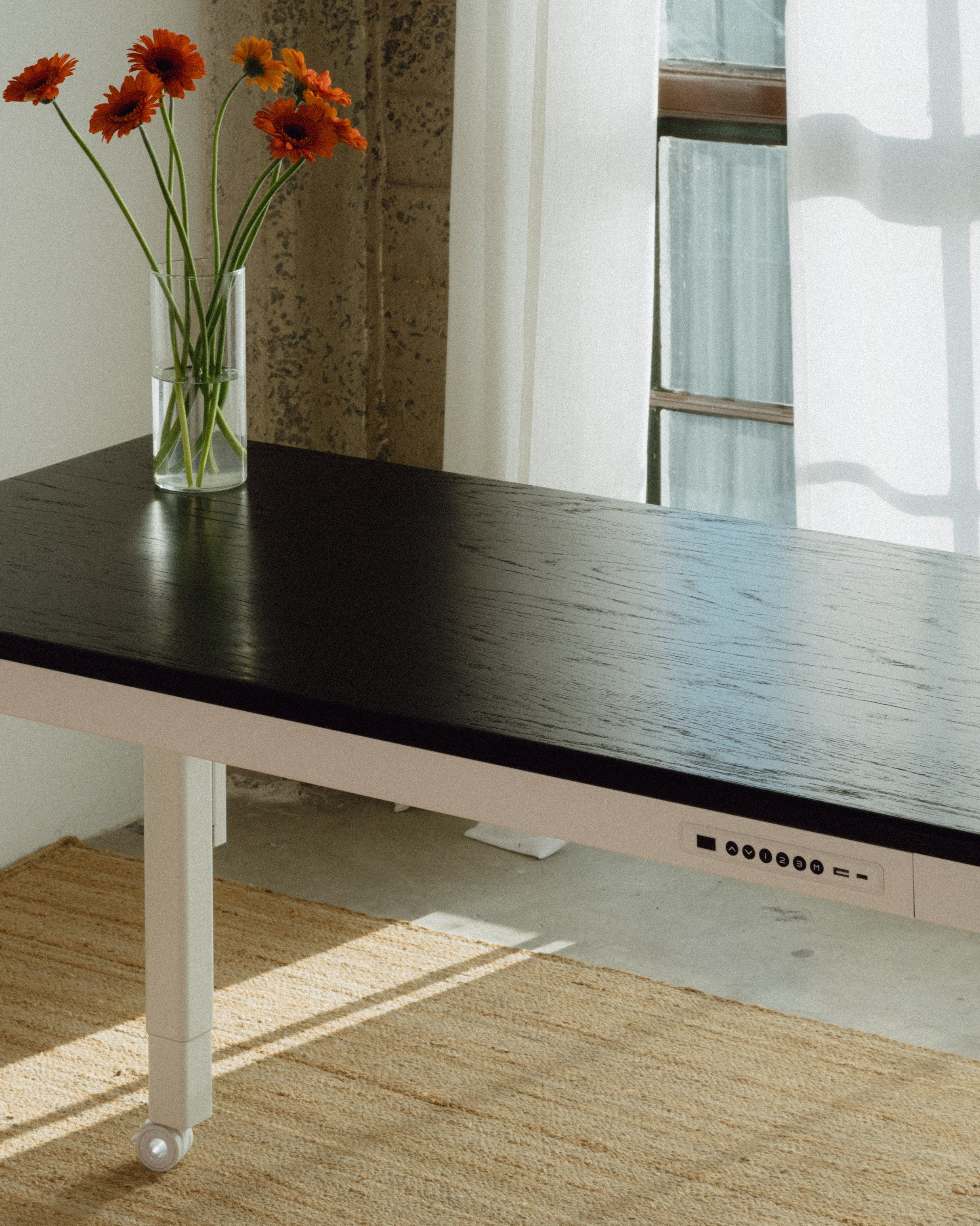 Ebony oak desktop standing desk with a vase of flowers in a room with a window and curtains.
