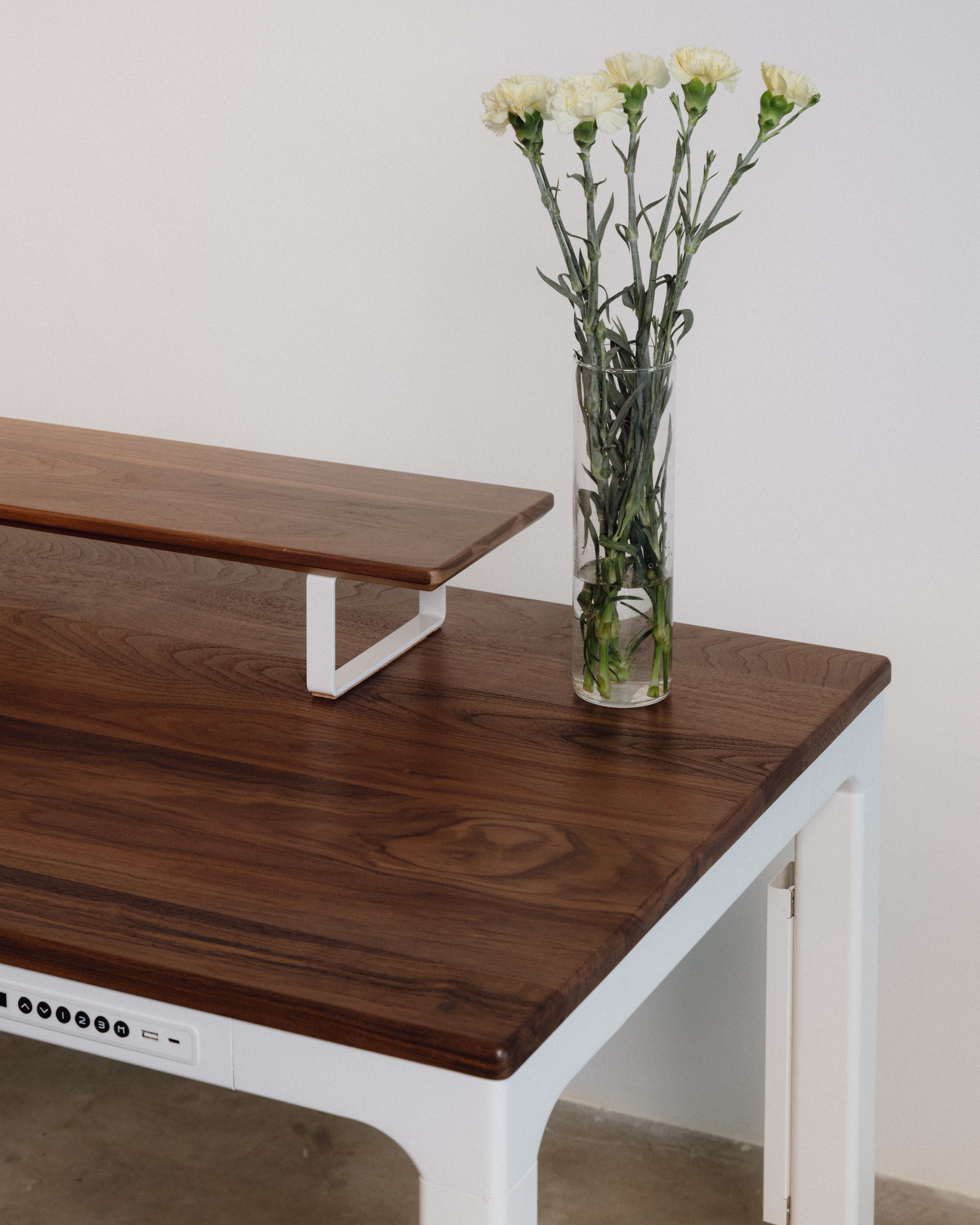 walnut desktop white frame standing desk with a vase of flowers on a plain background