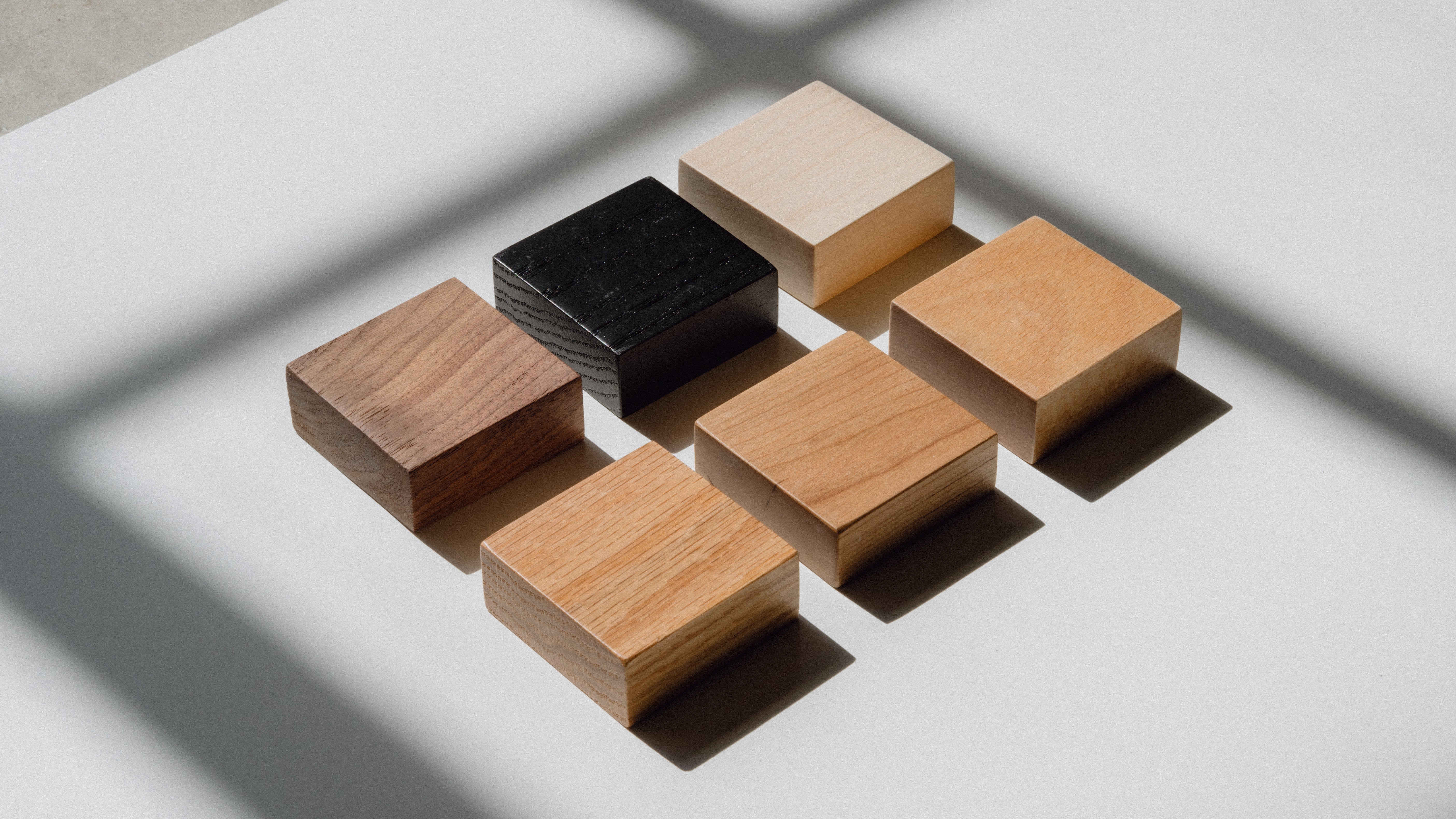 Three square wooden samples in different colors on a neutral background
